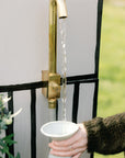 Brass outdoor water faucet mounted to wall and attached to garden hose
