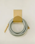 Modern brass hose holder in raw brass with garden hose coiled 