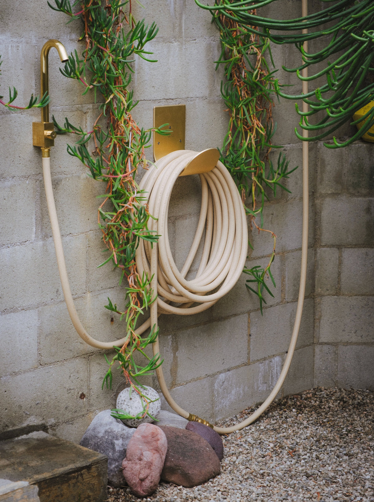 Hose hook in raw brass mounted on a wall with garden hose and faucet