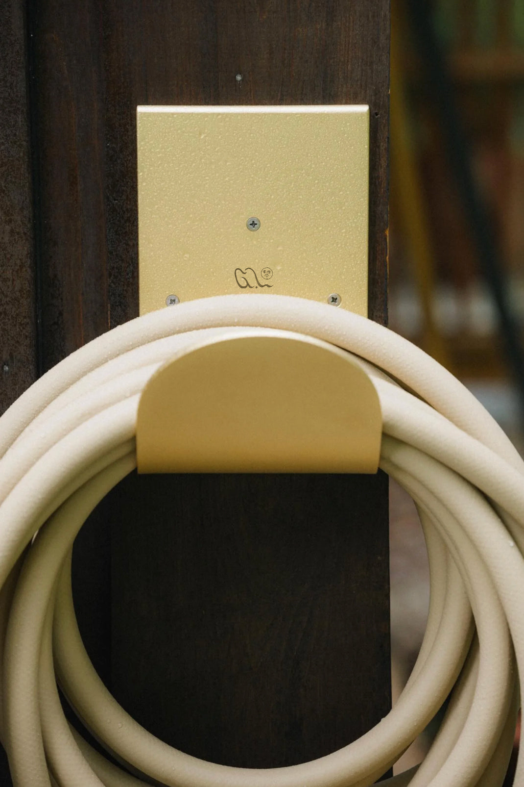 Metal wall mounted hose hanger in brass with garden hose